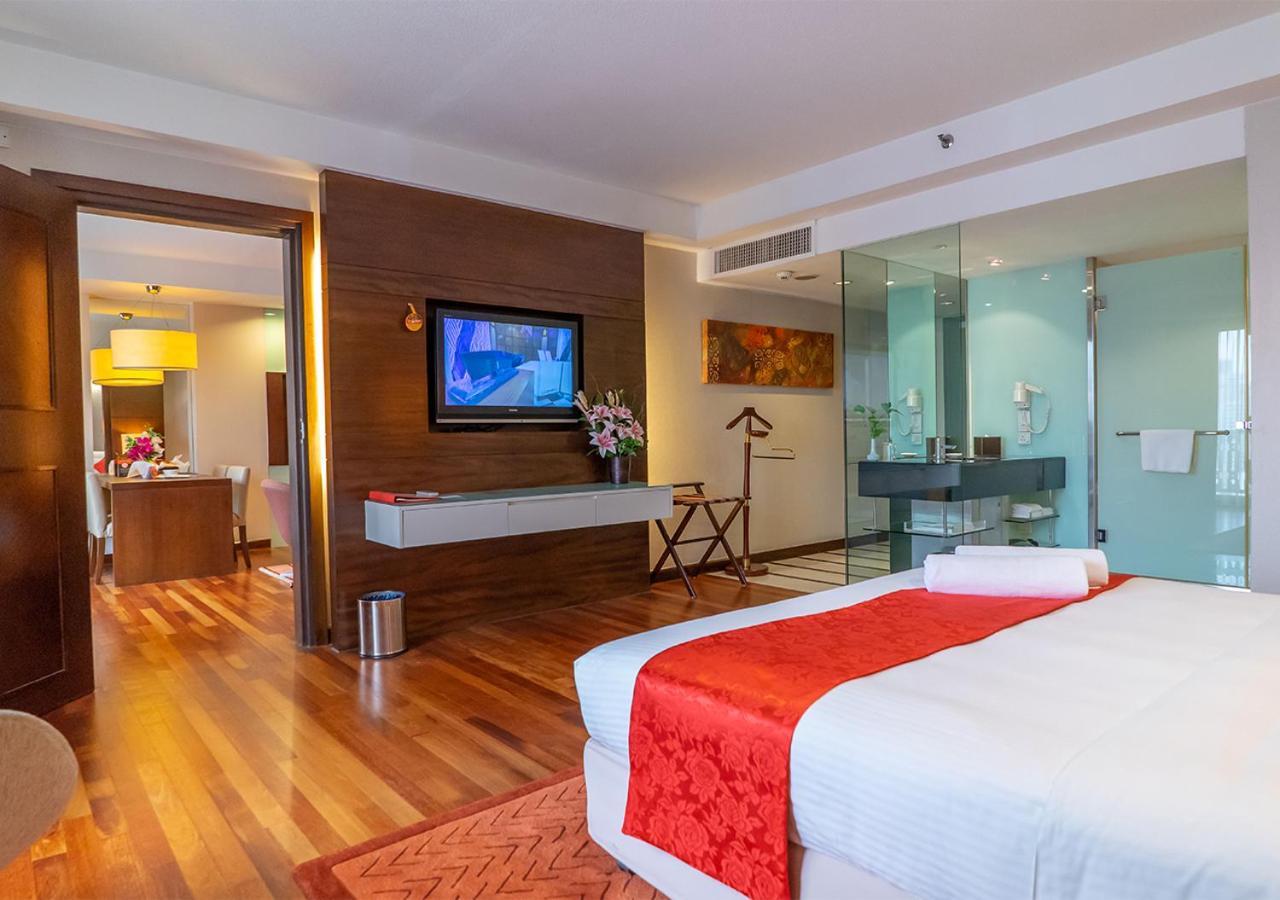 Seri Pacific Hotel Куала-Лумпур Экстерьер фото The photo shows a hotel room or suite featuring a modern and stylish interior. There is a large bed with white linens and a red decorative blanket. A wooden floor adds warmth to the space. In front of the bed, a television is mounted on the wall, and