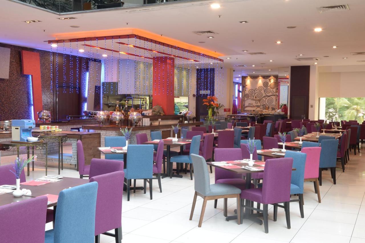 Seri Pacific Hotel Куала-Лумпур Экстерьер фото The photo shows the interior of a restaurant. It features a spacious dining area with a mix of purple and blue chairs arranged around wooden tables. The setting is modern and colorful, with bright lighting and decorative elements such as floral arran