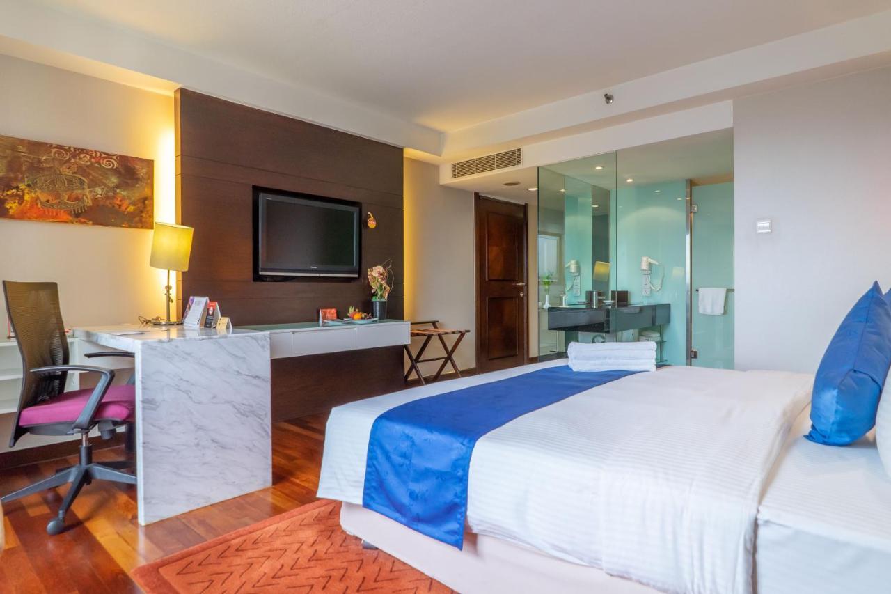 Seri Pacific Hotel Куала-Лумпур Экстерьер фото The photo shows a modern hotel room featuring:

- A large bed with white linens and a blue accent pillow.
- A flat-screen television mounted on the wall opposite the bed.
- A desk area with a marble top and a chair, providing a work space.
- A small 