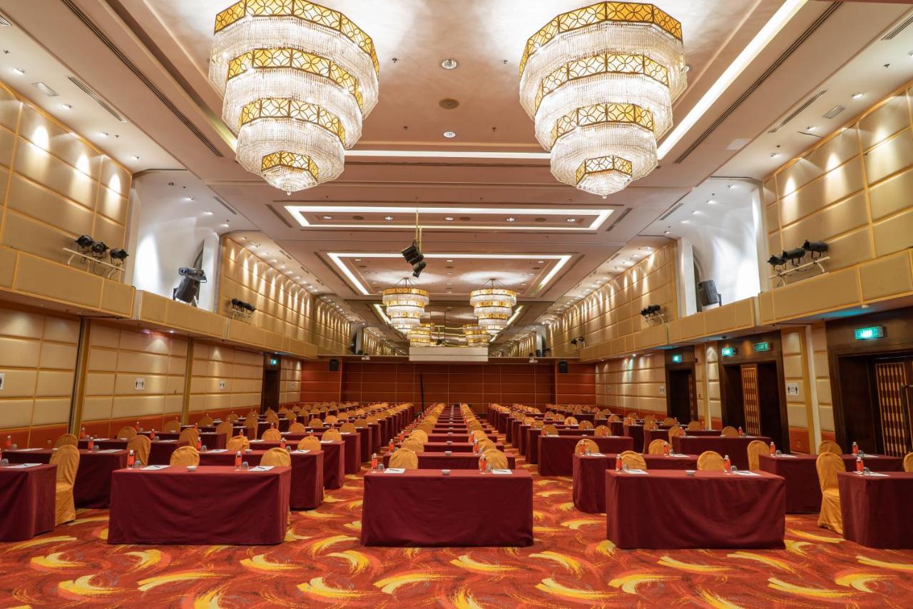 Seri Pacific Hotel Куала-Лумпур Экстерьер фото The image shows an elegantly designed conference or banquet hall. It features rows of tables, each adorned with red tablecloths, and there are chairs set around them. The room is well-lit with large, ornate chandeliers hanging from the ceiling, creat
