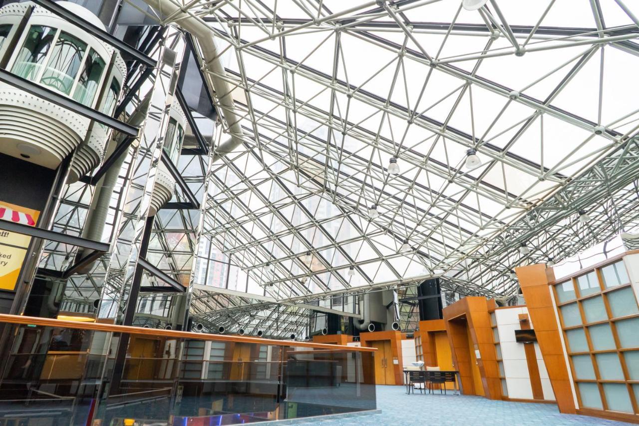 Seri Pacific Hotel Куала-Лумпур Экстерьер фото The photo depicts a modern architectural interior featuring a spacious atrium with a striking glass and steel roof. The roof consists of a series of geometric triangles, allowing natural light to flood the space. The interior design shows a combinati