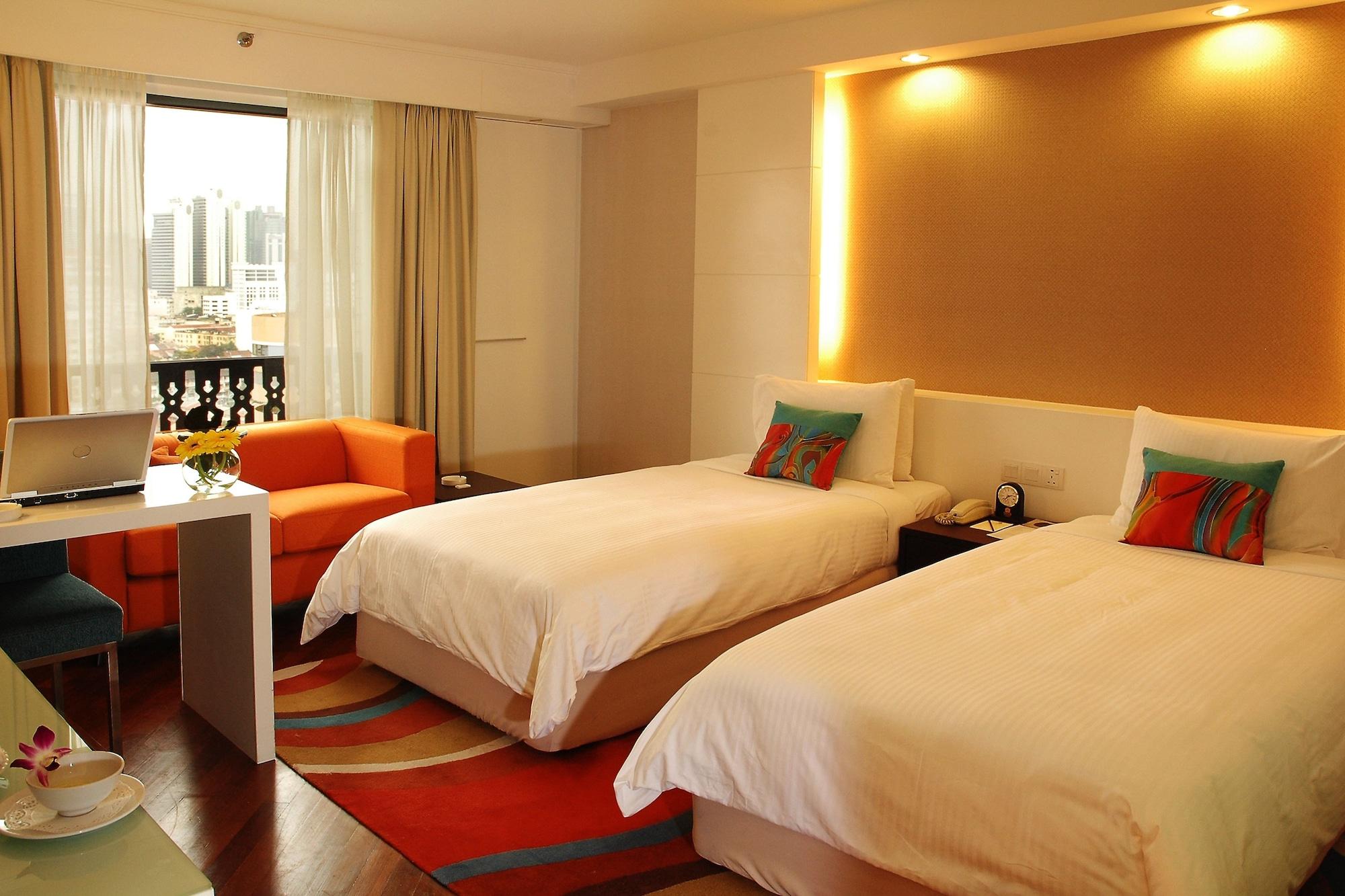 Seri Pacific Hotel Куала-Лумпур Номер фото The photo shows a modern hotel room featuring two single beds with white bedding. There is a cozy orange sofa in one corner and a small table with a laptop on it. The room has large windows with curtains that allow natural light to brighten the space