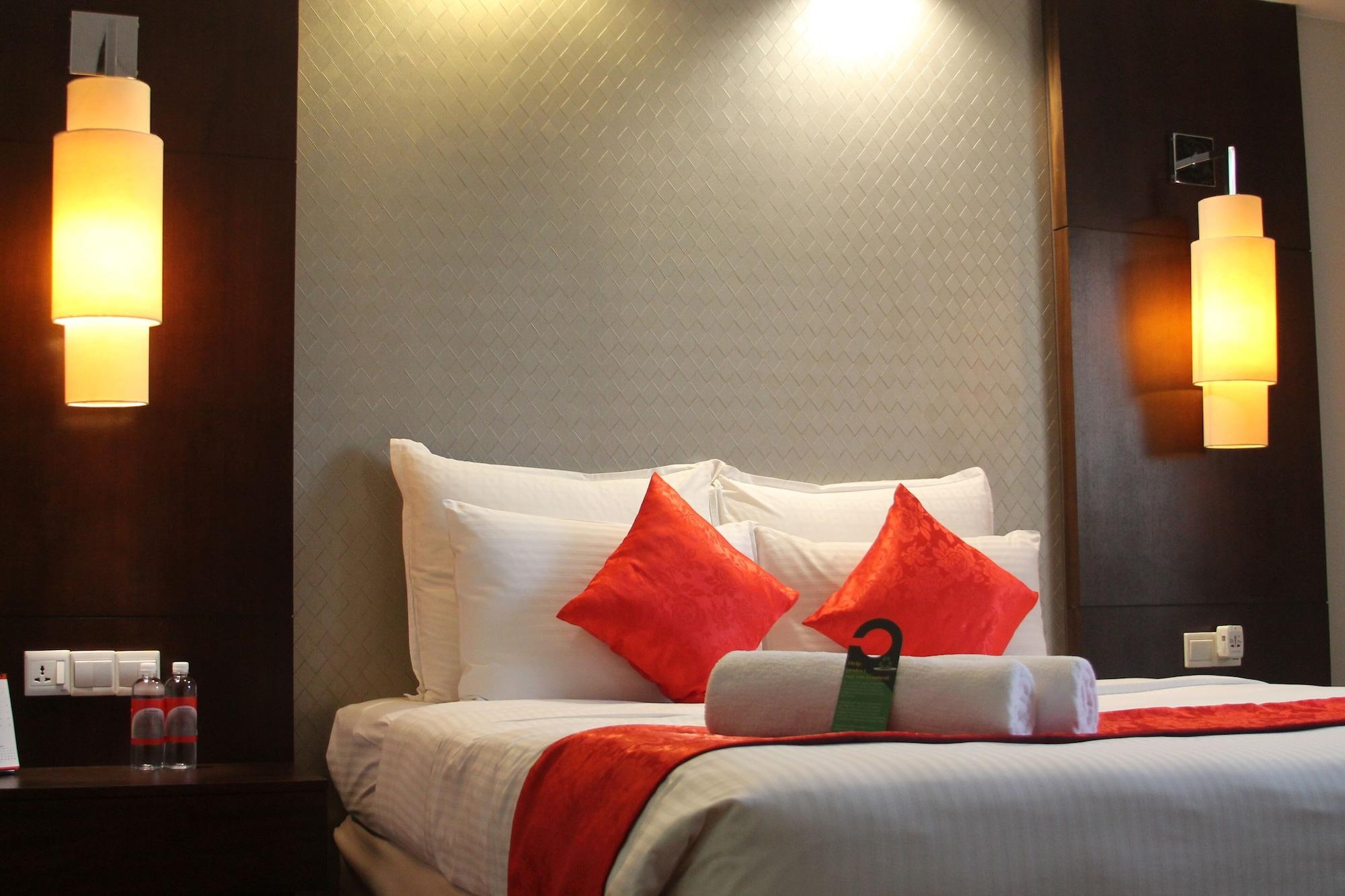 Seri Pacific Hotel Куала-Лумпур Экстерьер фото The photo shows a cozy hotel room with a neatly made bed featuring white linens and decorative red accent pillows. The headboard is dark wood, and on either side of the bed, there are softly glowing wall lamps. At the foot of the bed, there are rolle