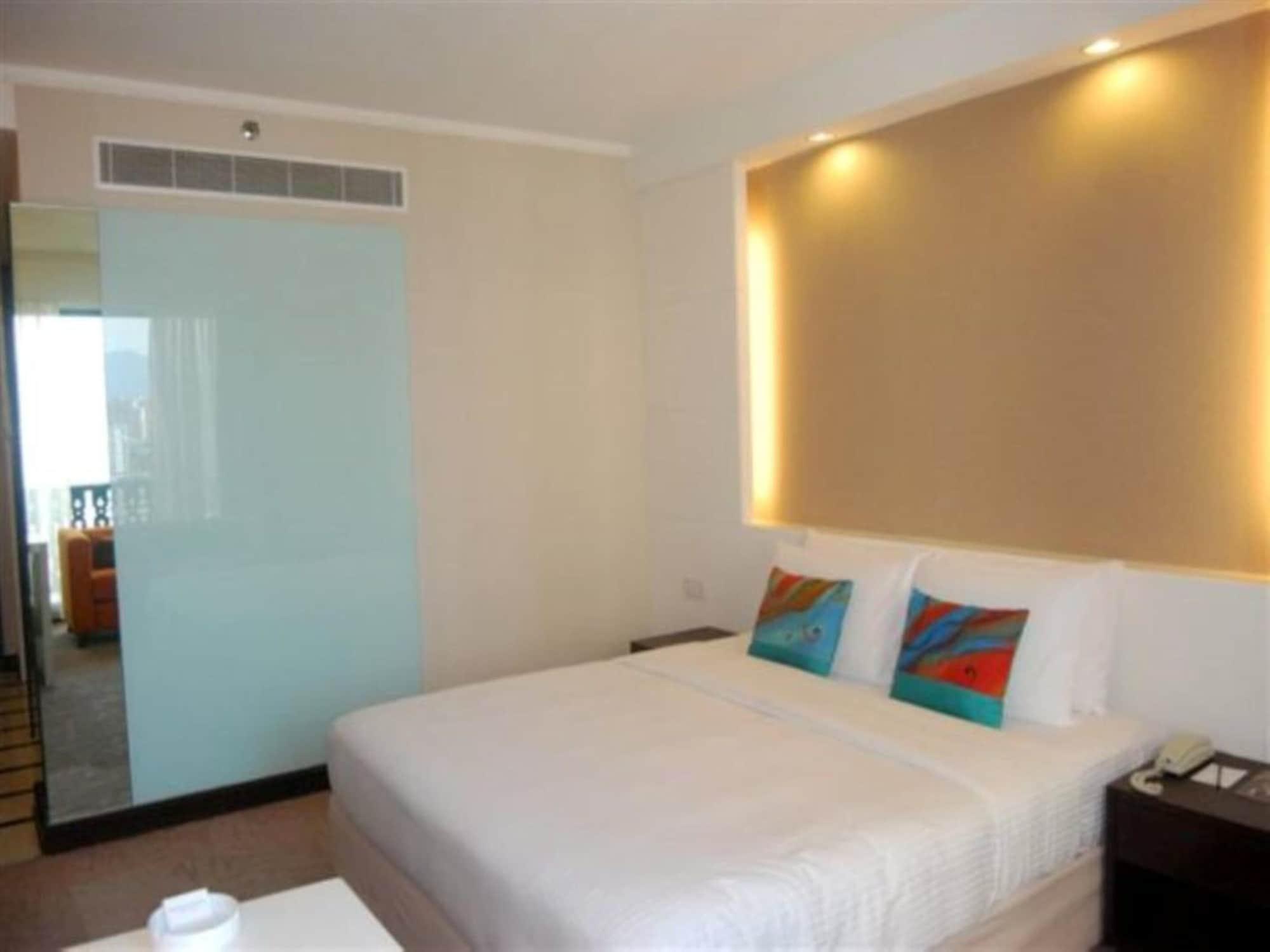 Seri Pacific Hotel Куала-Лумпур Экстерьер фото The image features a hotel room with a modern and minimalist design. It includes a large bed with white linens and colorful decorative pillows. The wall behind the bed has a soft, illuminated panel that adds warmth to the space. On one side of the ro