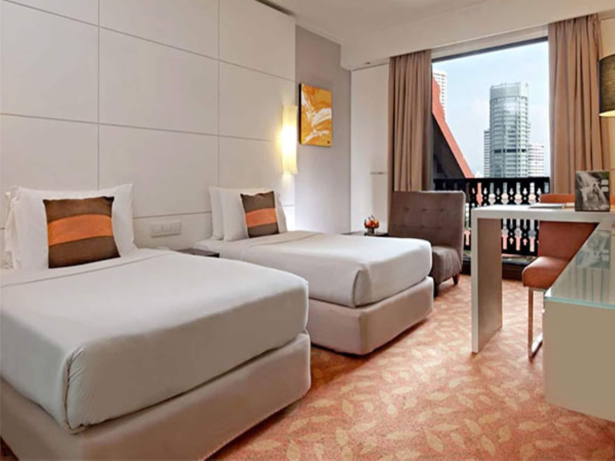Seri Pacific Hotel Куала-Лумпур Экстерьер фото The photo shows a contemporary hotel room featuring two twin beds with light-colored bedding and decorative pillows. There's a small seating area with an armchair, and a desk with a clear top. Large windows allow natural light to enter, providing a v