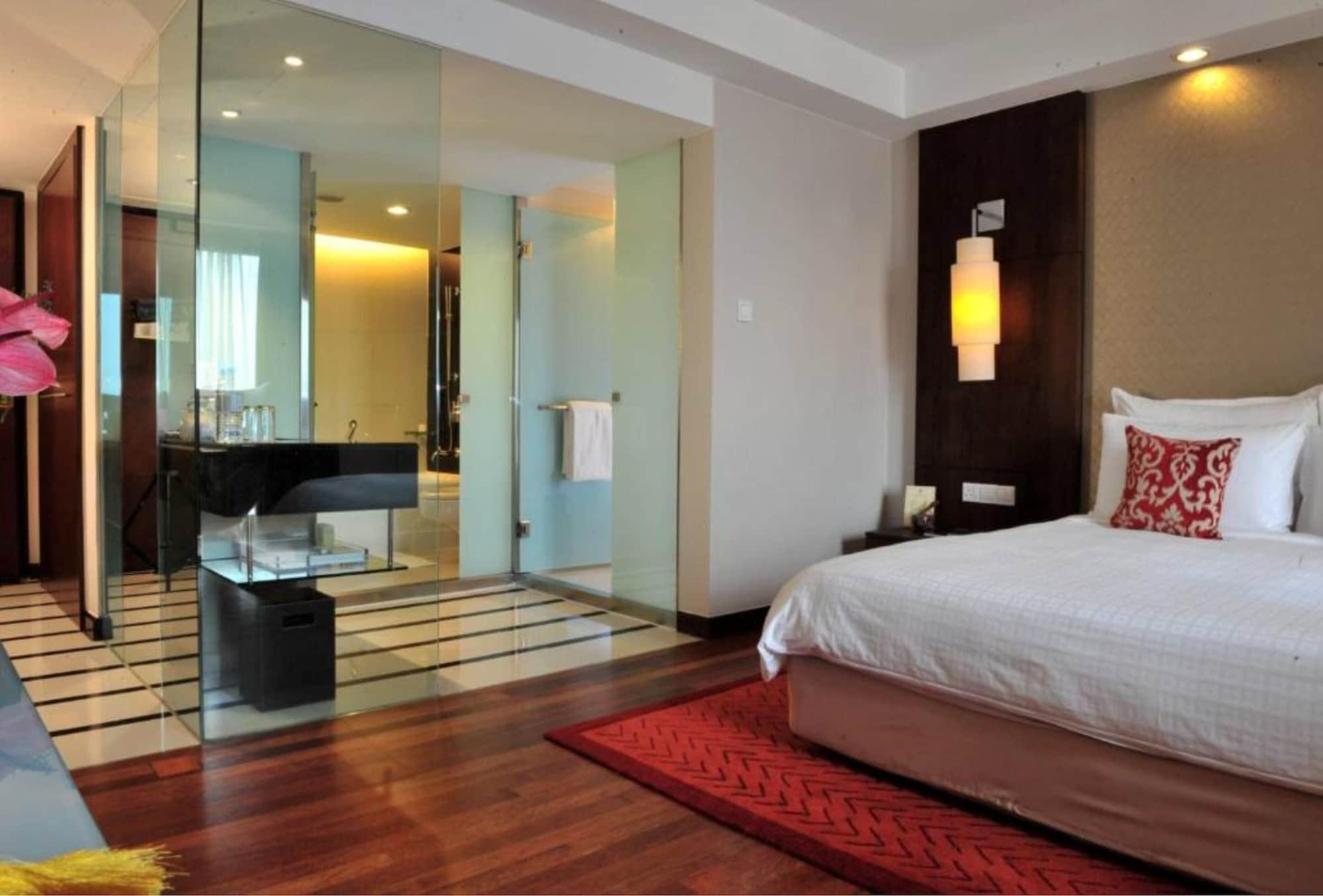 Seri Pacific Hotel Куала-Лумпур Экстерьер фото The photo shows a modern hotel room featuring a stylish decor. On one side, there is a bed with white linens and a decorative red and white pillow. The flooring is wooden, complemented by a red area rug. 

Adjacent to the bed, there is a glass partit