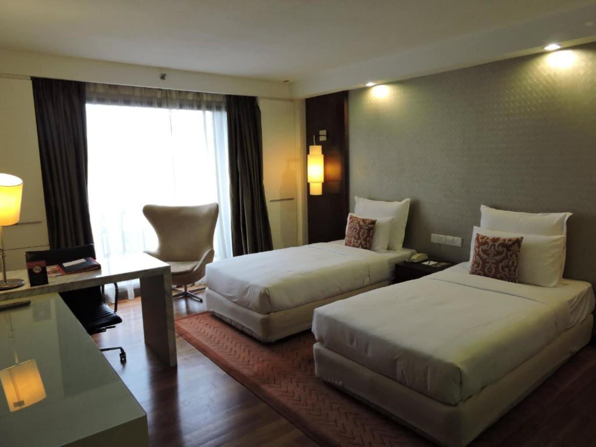 Seri Pacific Hotel Куала-Лумпур Экстерьер фото The photo shows a modern hotel room with two single beds positioned side by side. Each bed has white linens and a decorative pillow. There is a large window with sheer curtains allowing natural light to brighten the space. A comfortable chair is posi