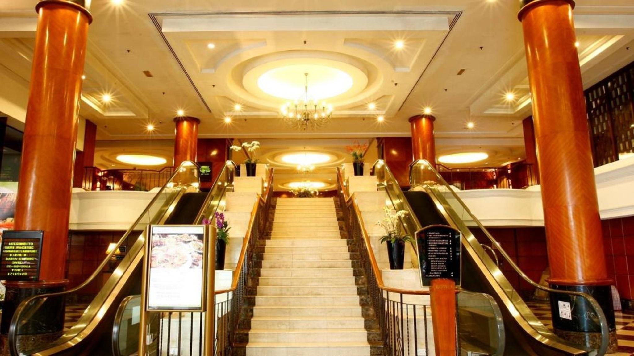 Seri Pacific Hotel Куала-Лумпур Экстерьер фото The photo shows the interior of a grand hotel lobby. There is a large staircase in the center, flanked by escalators on both sides. The staircase is made of marble and leads to a higher level, while the escalators appear to provide access to the same