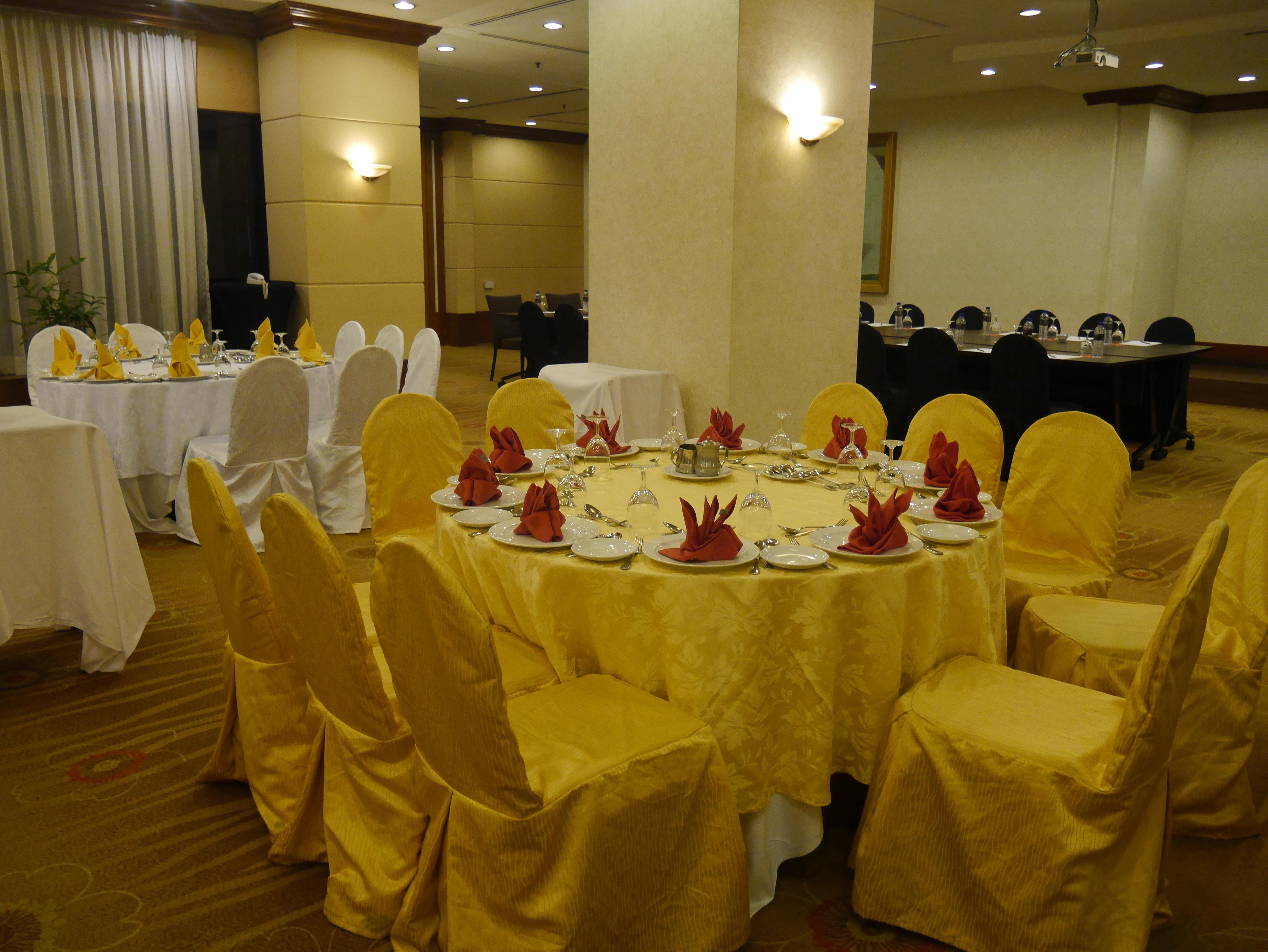 Seri Pacific Hotel Куала-Лумпур Экстерьер фото The photo shows a banquet or dining area set up for an event. There are several tables covered with white and yellow tablecloths. The table in the foreground features chairs with yellow covers and is adorned with neatly arranged plates, utensils, and