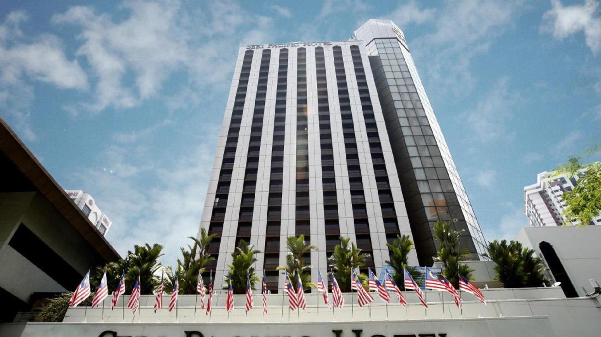 Seri Pacific Hotel Куала-Лумпур Экстерьер фото The photo shows a tall modern building with a predominantly glass facade. The structure has a sleek design and appears to be several stories high. In the foreground, there are multiple flags on display, likely representing the United States, as they 