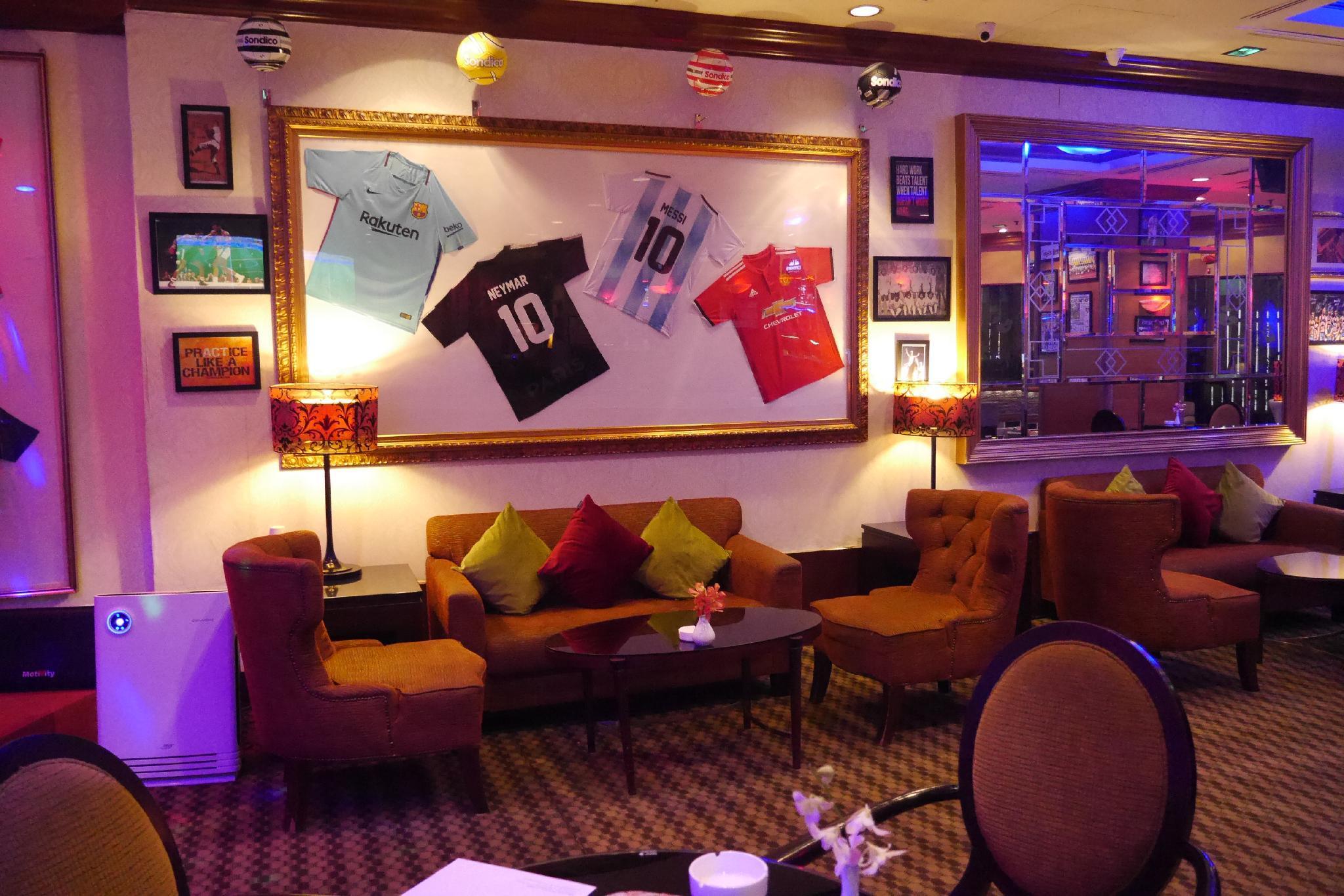 Seri Pacific Hotel Куала-Лумпур Экстерьер фото The photo shows a cozy lounge area decorated with several football jerseys displayed on a wall. The jerseys are hung in a framed arrangement and feature different colors, including light blue, black, red, and sky blue. Below the jerseys, there are tw