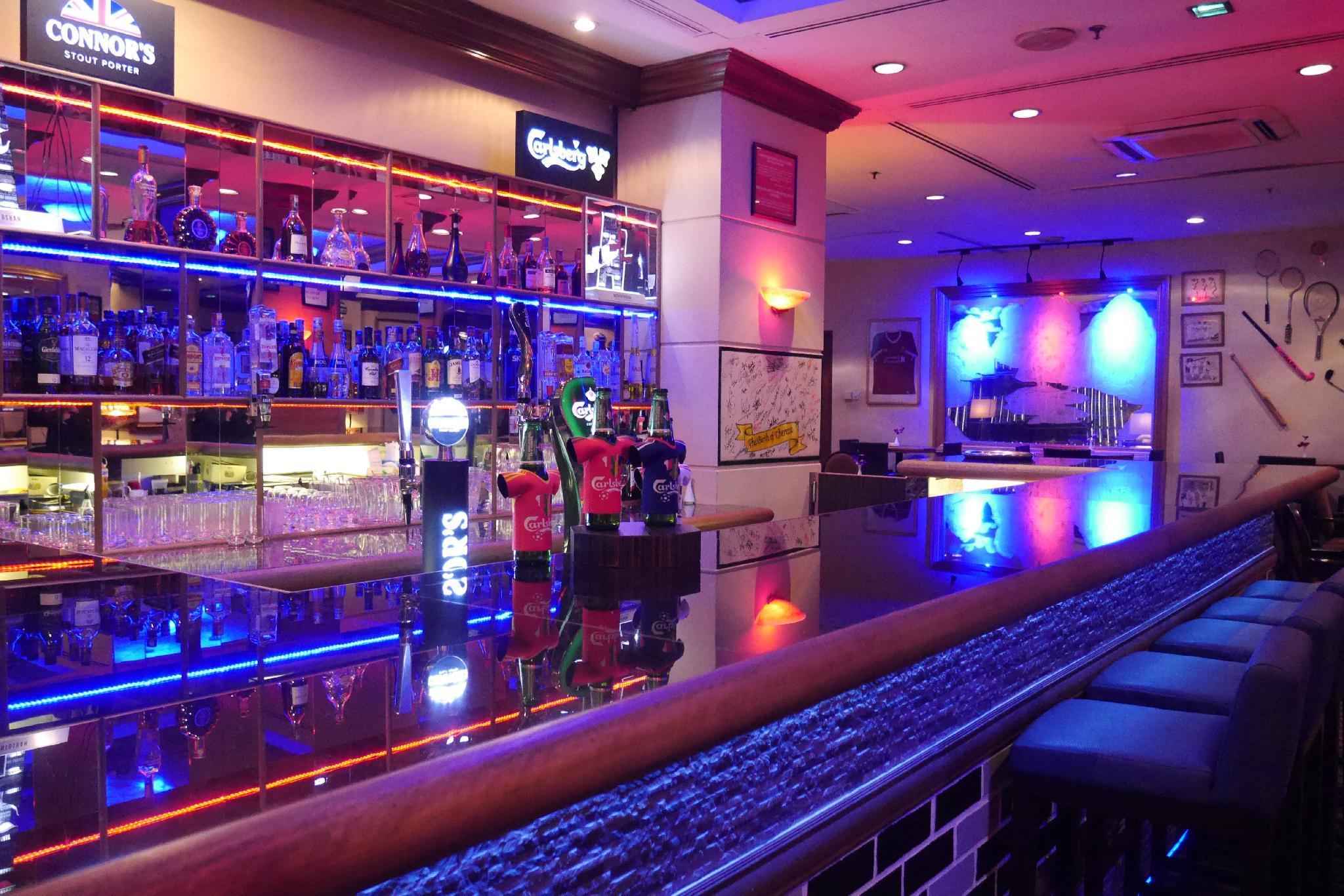 Seri Pacific Hotel Куала-Лумпур Экстерьер фото The image depicts a stylish bar interior. On the left side, there is a well-stocked bar counter with a variety of bottles of alcohol displayed on shelves, illuminated by colorful LED lights creating a vibrant atmosphere. The overall decor includes mo