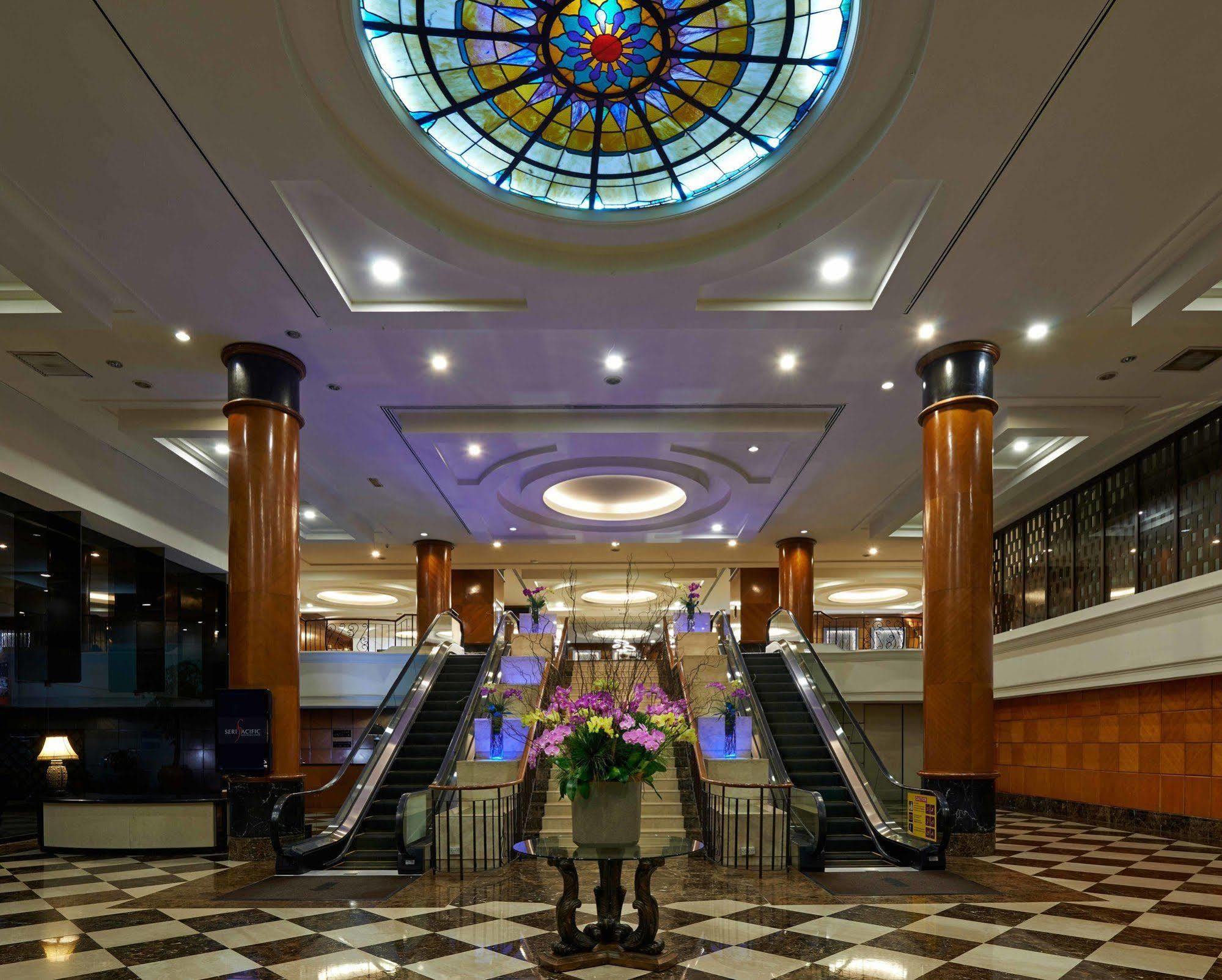 Seri Pacific Hotel Куала-Лумпур Экстерьер фото The photo depicts an elegant hotel lobby featuring a large stained glass ceiling that adds a colorful touch to the space. The lobby has polished marble flooring with a checkerboard pattern. In the center, there is a beautiful arrangement of flowers i