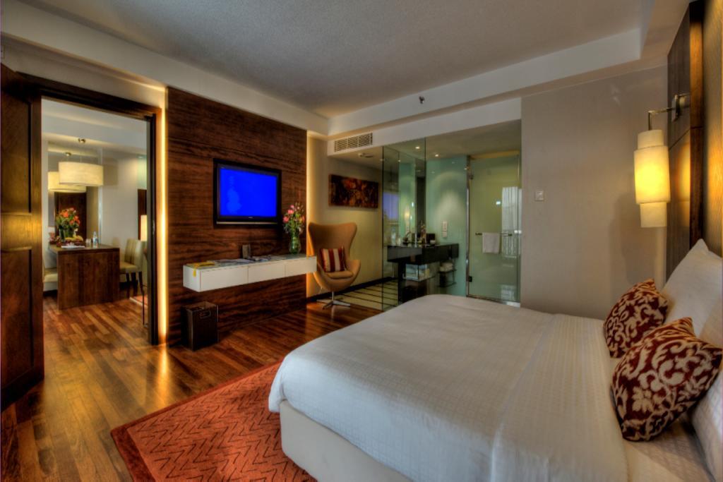 Seri Pacific Hotel Куала-Лумпур Экстерьер фото The photo shows a modern hotel room featuring a large bed with white linens and decorative pillows. There is wood flooring and an area rug in front of the bed. A flat-screen television is mounted on the wall, and next to it is a stylish wooden dresse