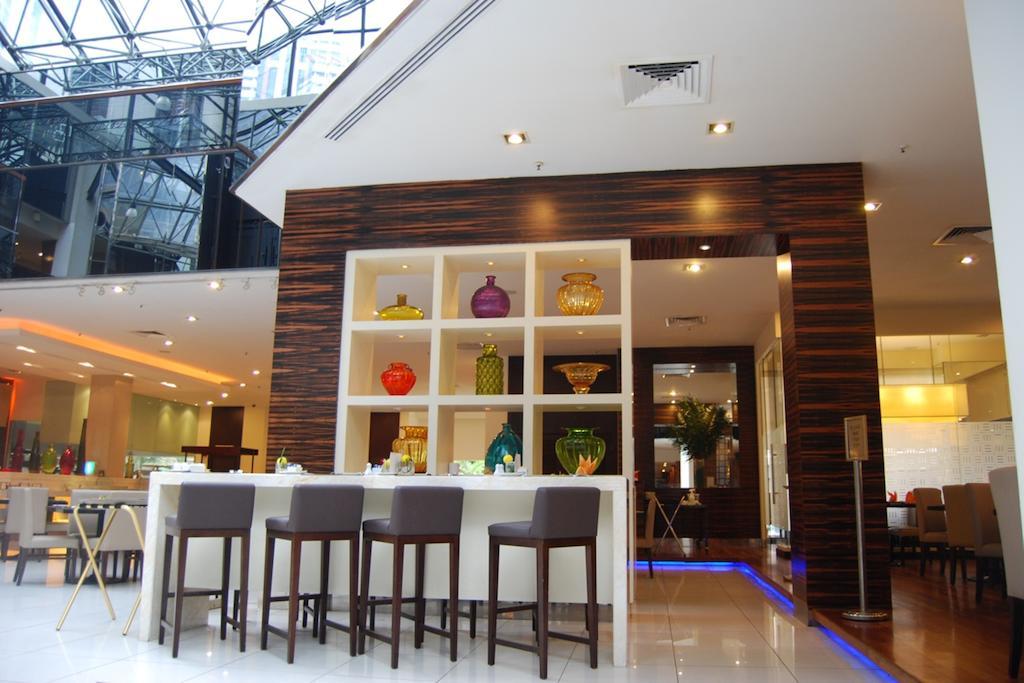 Seri Pacific Hotel Куала-Лумпур Экстерьер фото The image shows an interior space, likely a modern restaurant or hotel lobby. There is a sleek bar area with several high stools arranged in front of a stylish back counter. Behind the bar, there are several shelves displaying colorful glassware and 