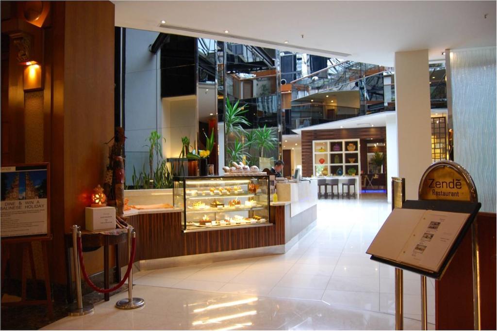 Seri Pacific Hotel Куала-Лумпур Экстерьер фото The photo shows the interior of a modern hotel or restaurant lobby. There is a large display case filled with various pastries or desserts, indicating a focus on food. The area is bright and spacious, with plants adding a touch of greenery. To the si